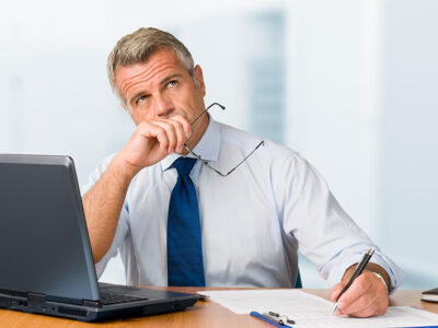Businessman at his desk writing and looking lost in thought.